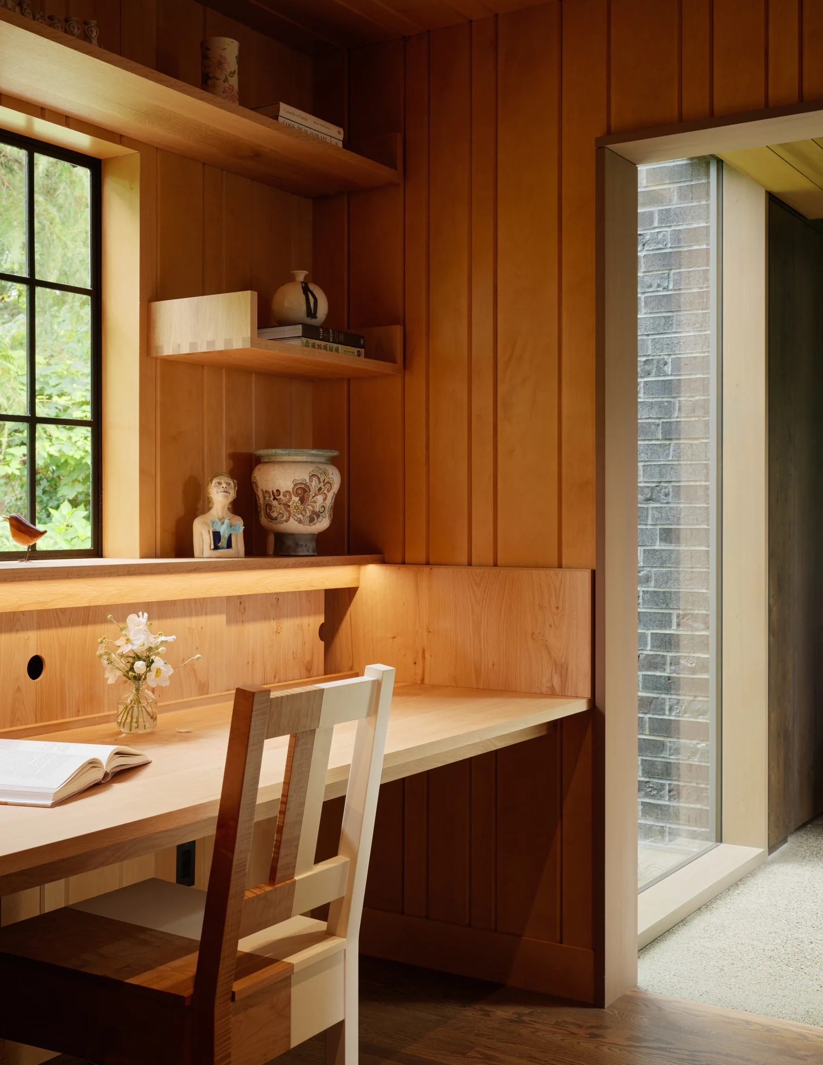 Desk area with wood paneling, built-in shelving, and a view through a window.