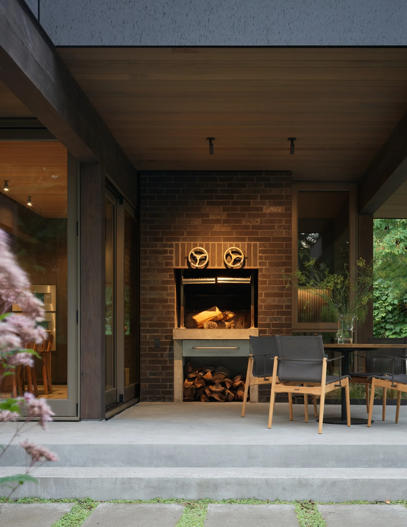 Covered patio area featuring a brick fireplace with wood storage and modern outdoor furniture.
