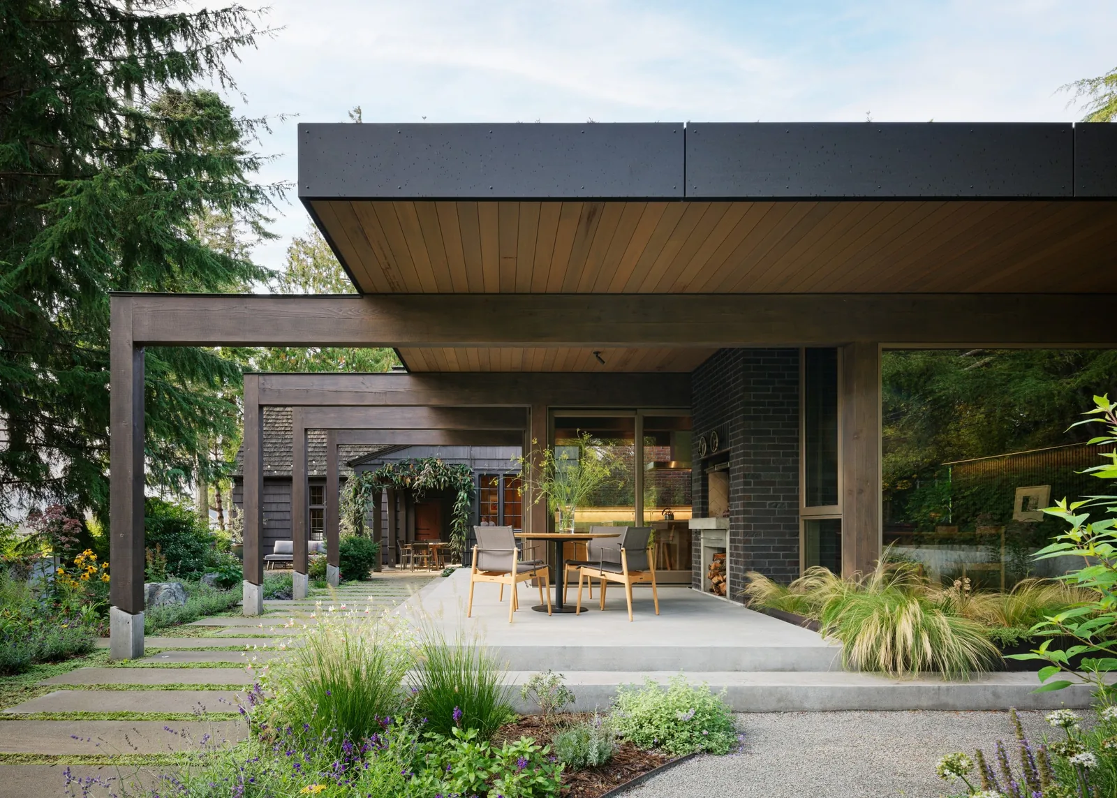 Covered patio with exposed wood beams and concrete flooring extending from the house into a landscaped garden.