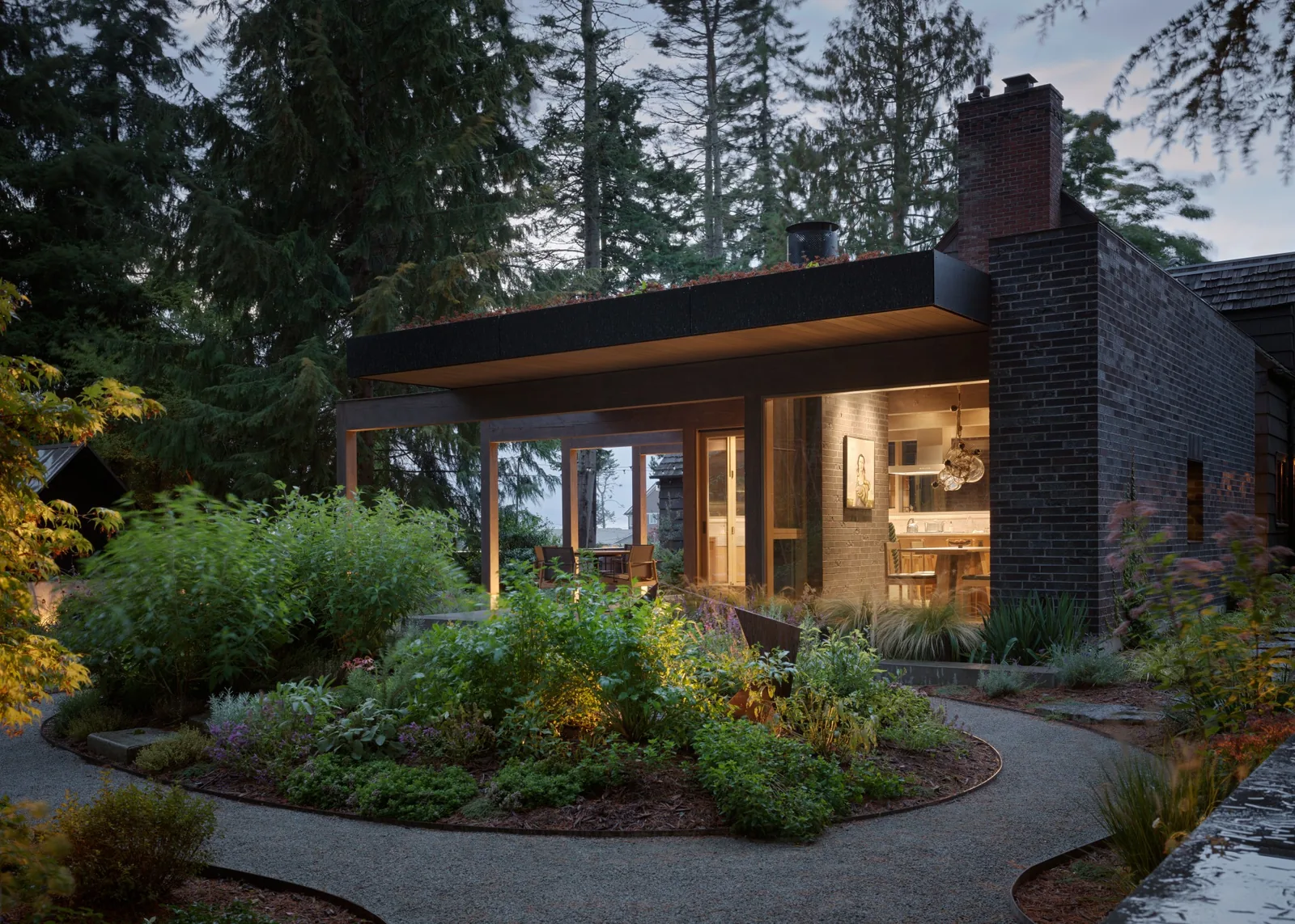 Modern house exterior with a covered patio and extensive landscaping at dusk.