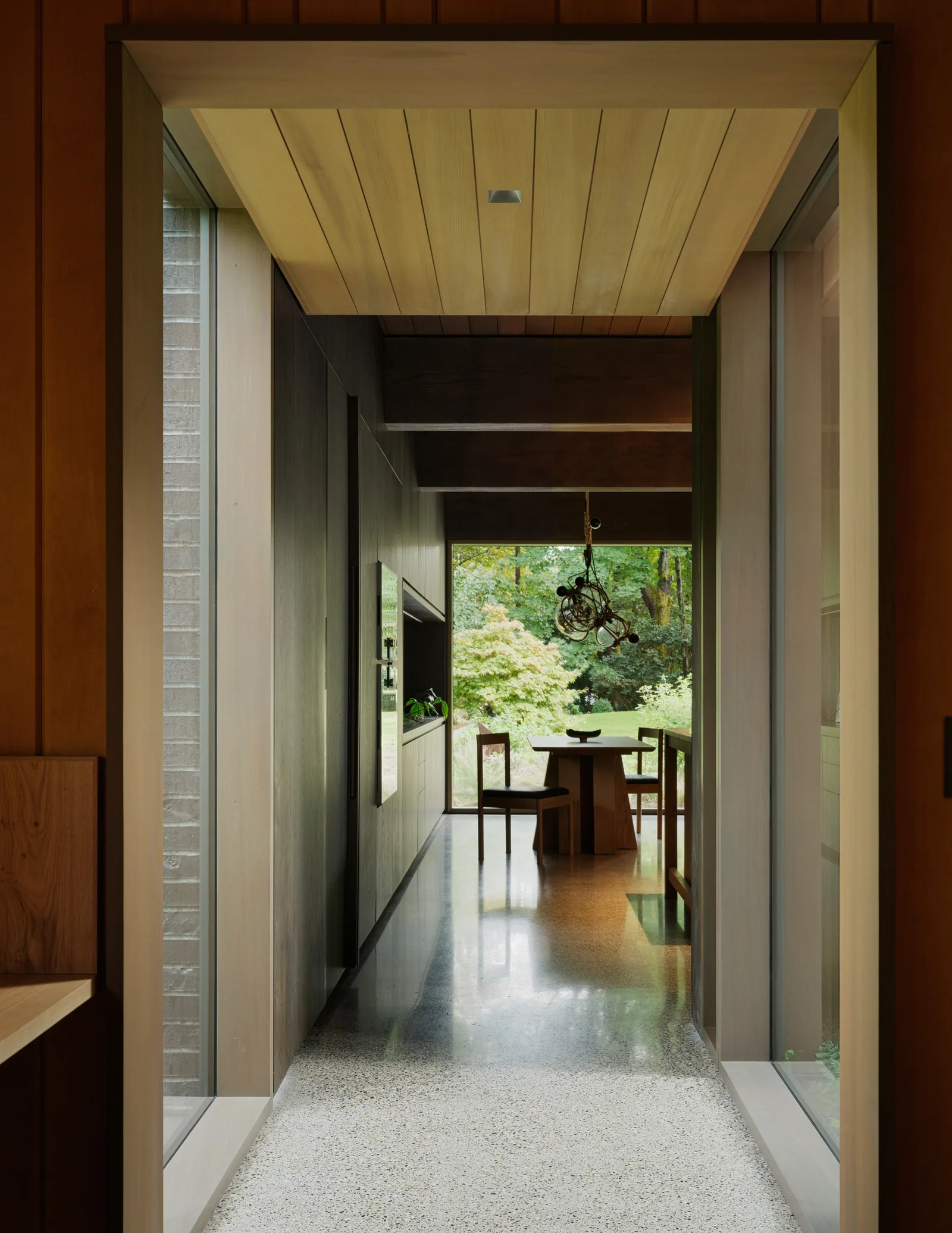 Interior corridor with terrazzo floor and wood-paneled walls leading to dining area with multiple large windows.