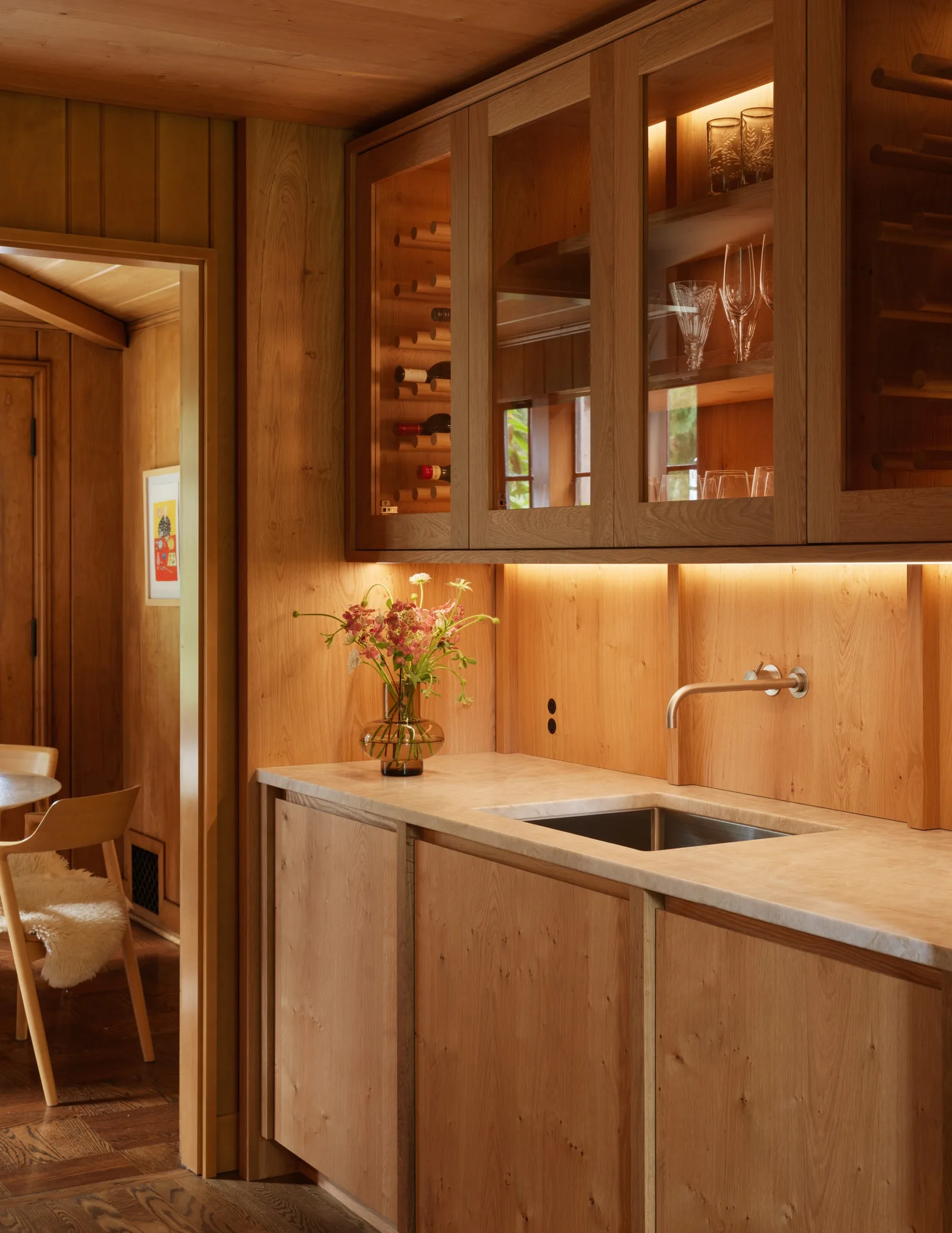 Kitchen space features wood cabinets with glass fronts, integrated lighting, and a built-in sink with wall-mounted faucet.