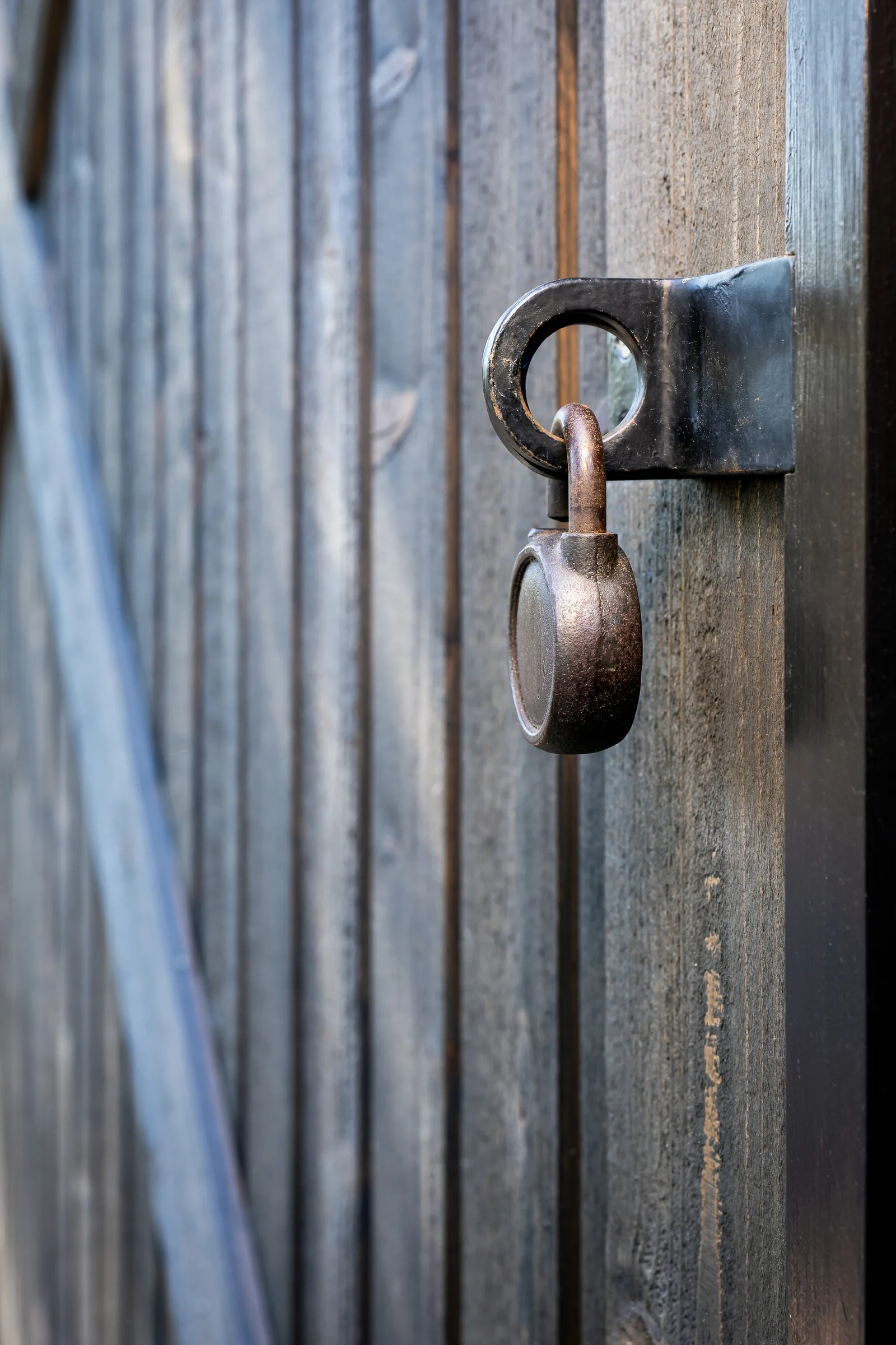 Rusted metal padlock securing a vertical wooden surface with black metal hasp.