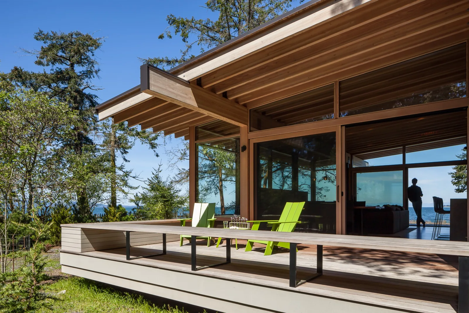 Modern house with a wooden deck and large glass sliding doors opening to a forested landscape.