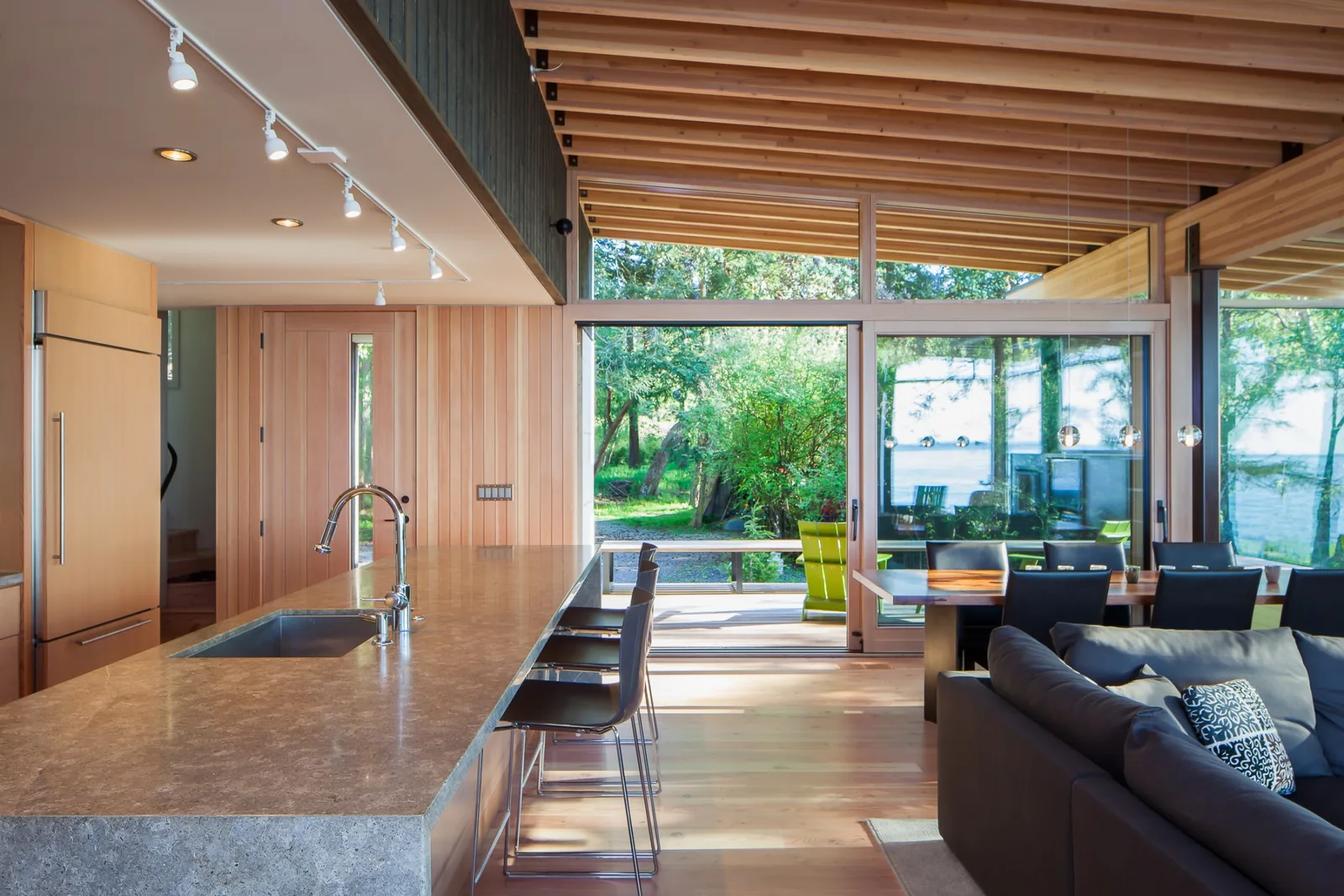 Open kitchen and dining room with floor-to-ceiling glass doors opening to outdoor greenery.
