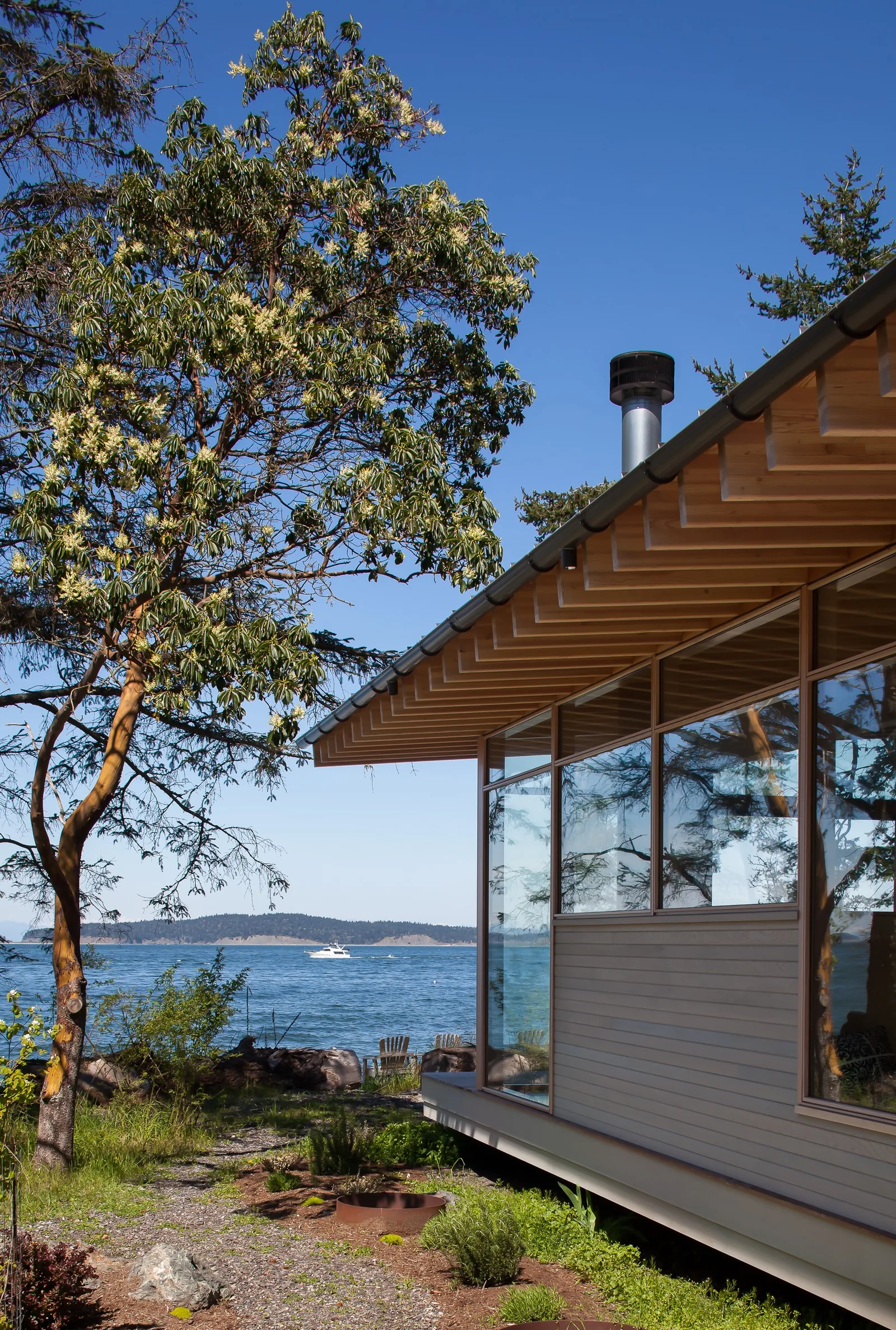 Side view of a modern lakeside house with extensive glass windows and a wooden roof overhang.