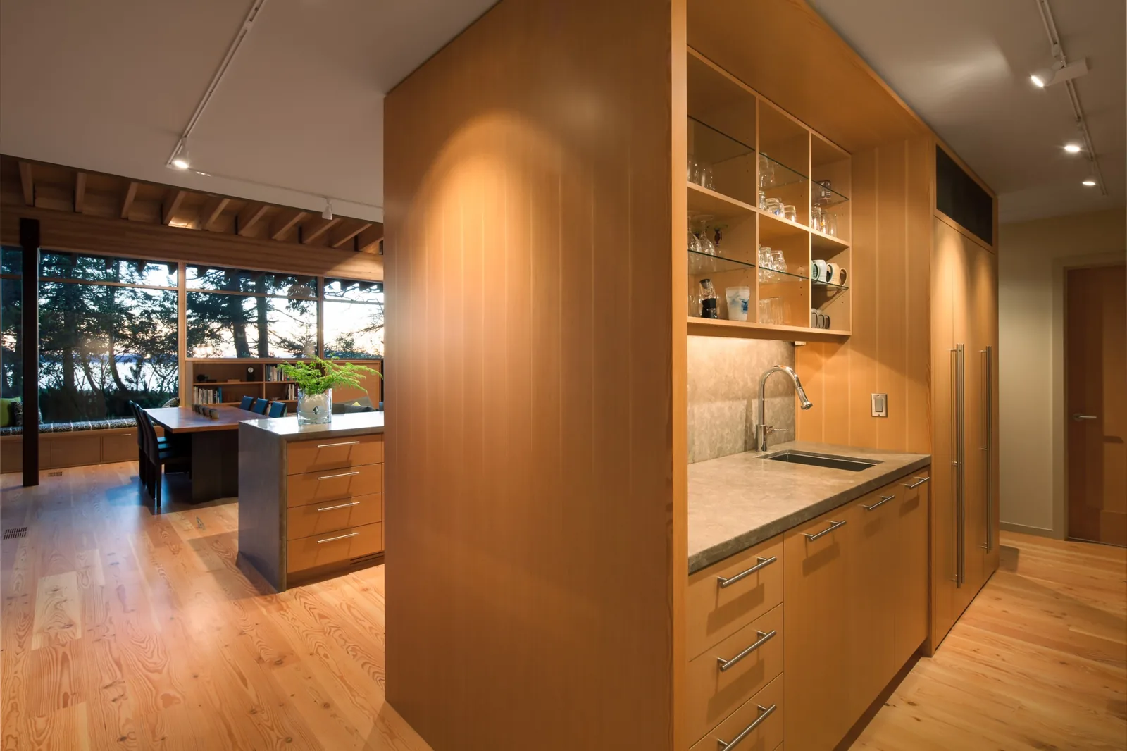 Kitchen and dining area with wood finishes, concrete countertop, and large windows in a contemporary home.