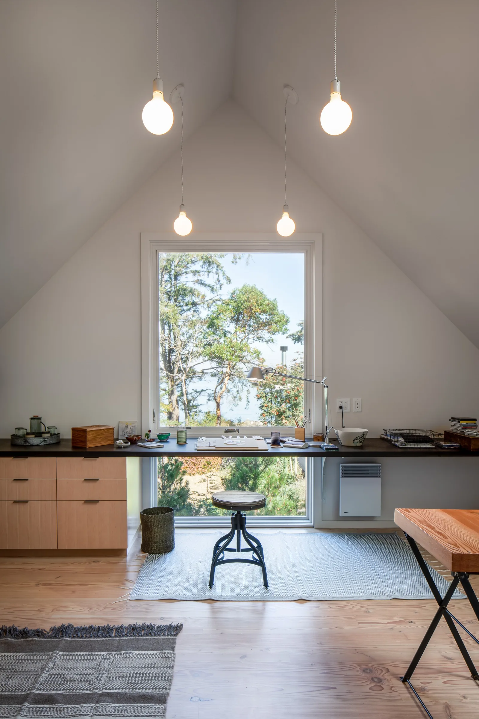 A workspace in a room with a steeply pitched ceiling, illuminated by hanging bulbs and natural light from a large window.