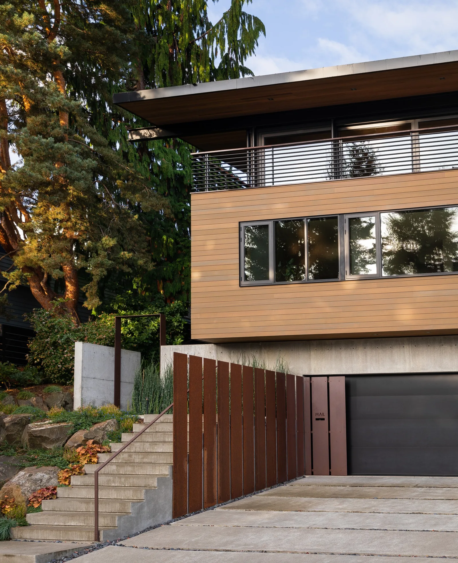 Exterior front view of a modern house featuring wood siding on the upper floor, concrete base, and a metal garage door.