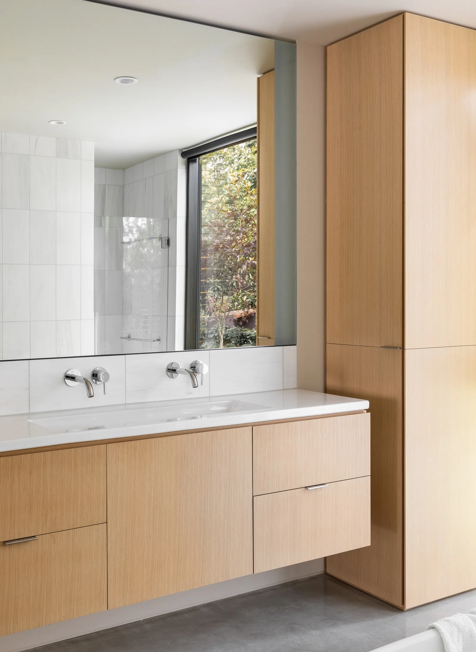 Bathroom features light wood cabinetry with a white countertop and wall-mounted faucets below a large mirror.