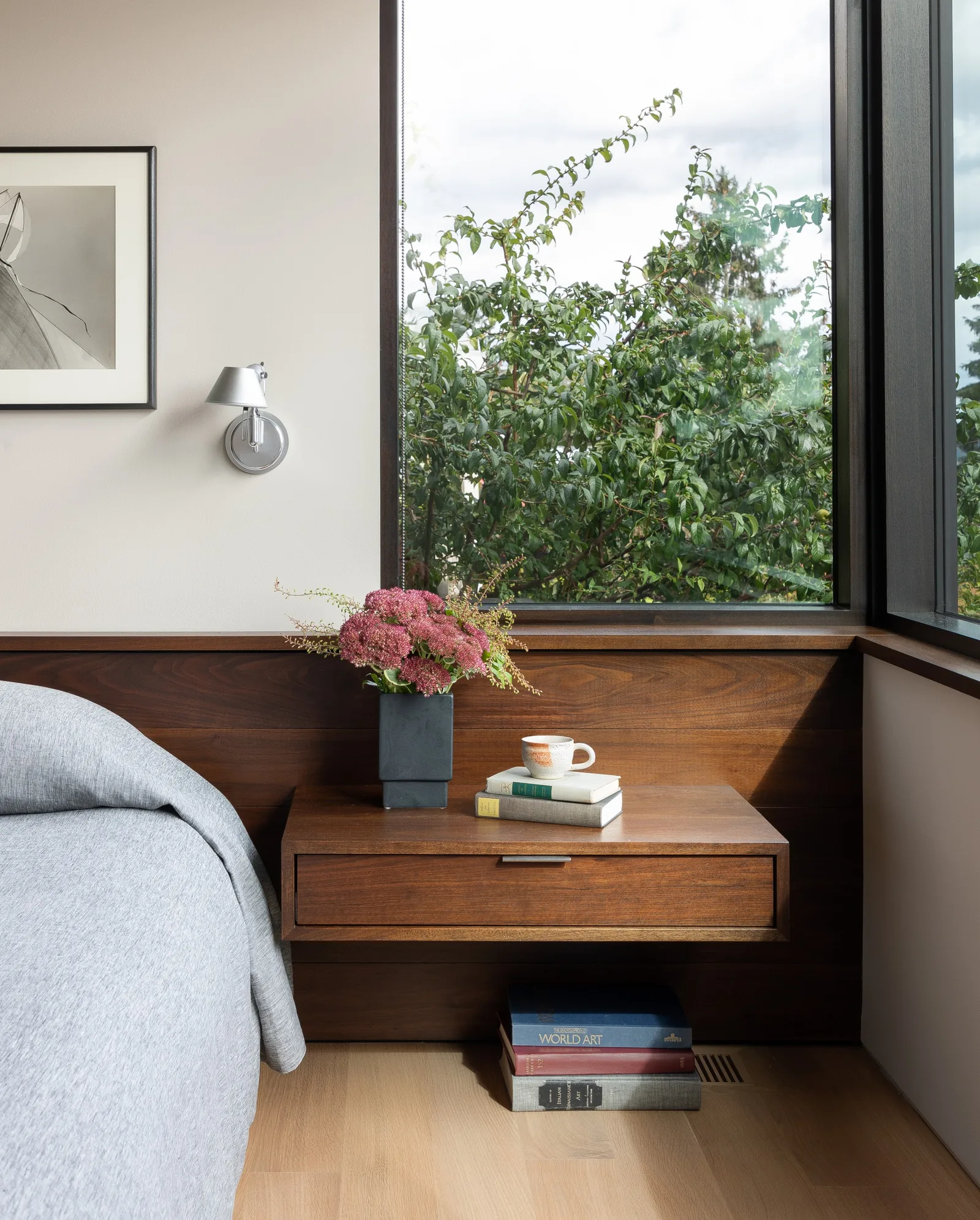 Wood-paneled bedroom corner with a floating nightstand beneath large corner windows.