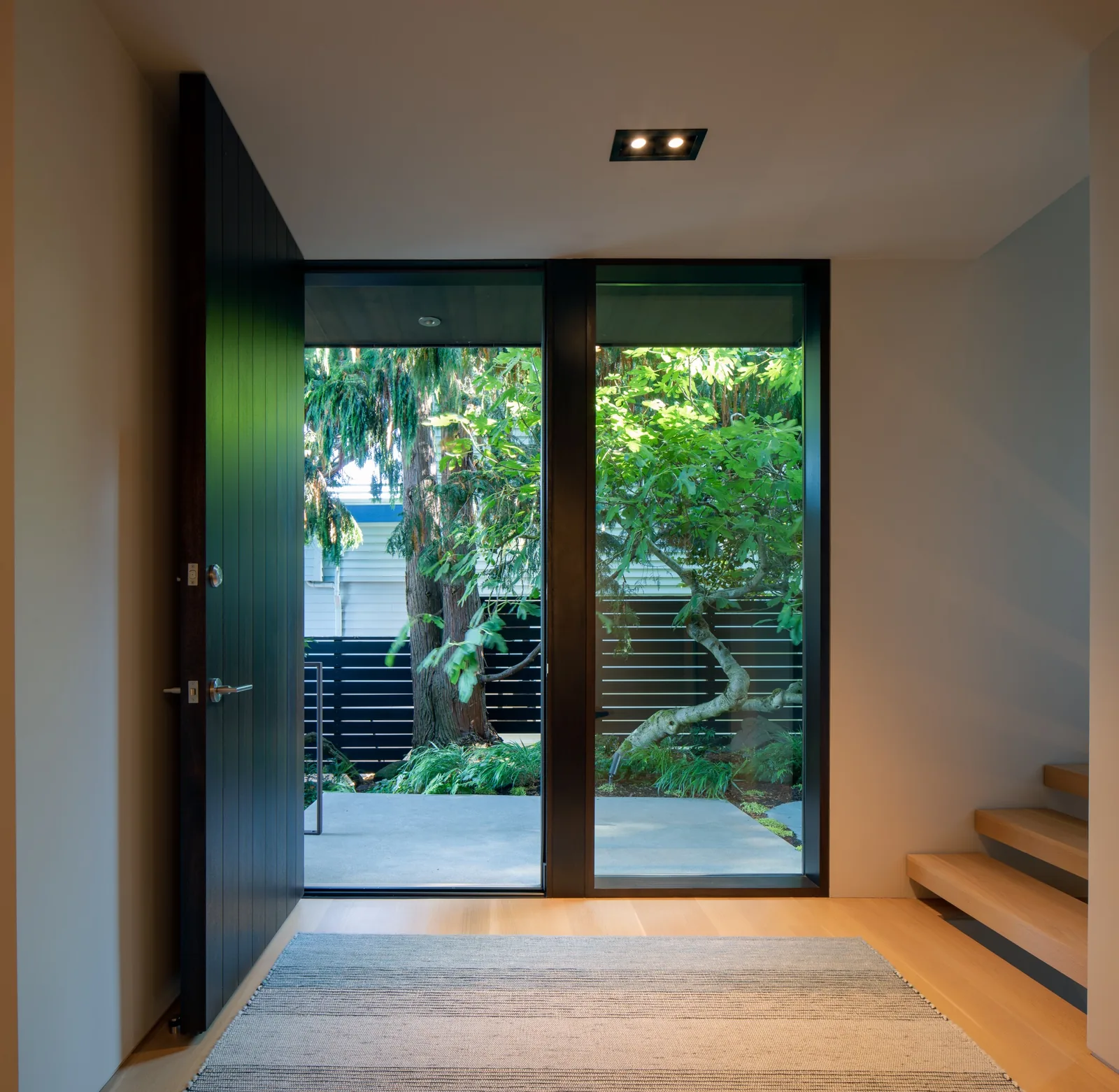 Entryway with a pivot door and floor-to-ceiling glazing opening to a garden outside.