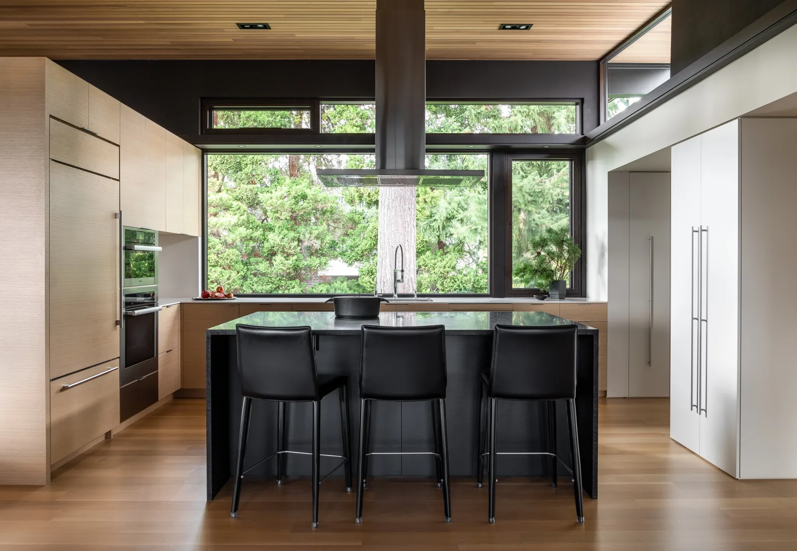 Kitchen features a black island with seating, light wood cabinetry, and large windows with transoms.