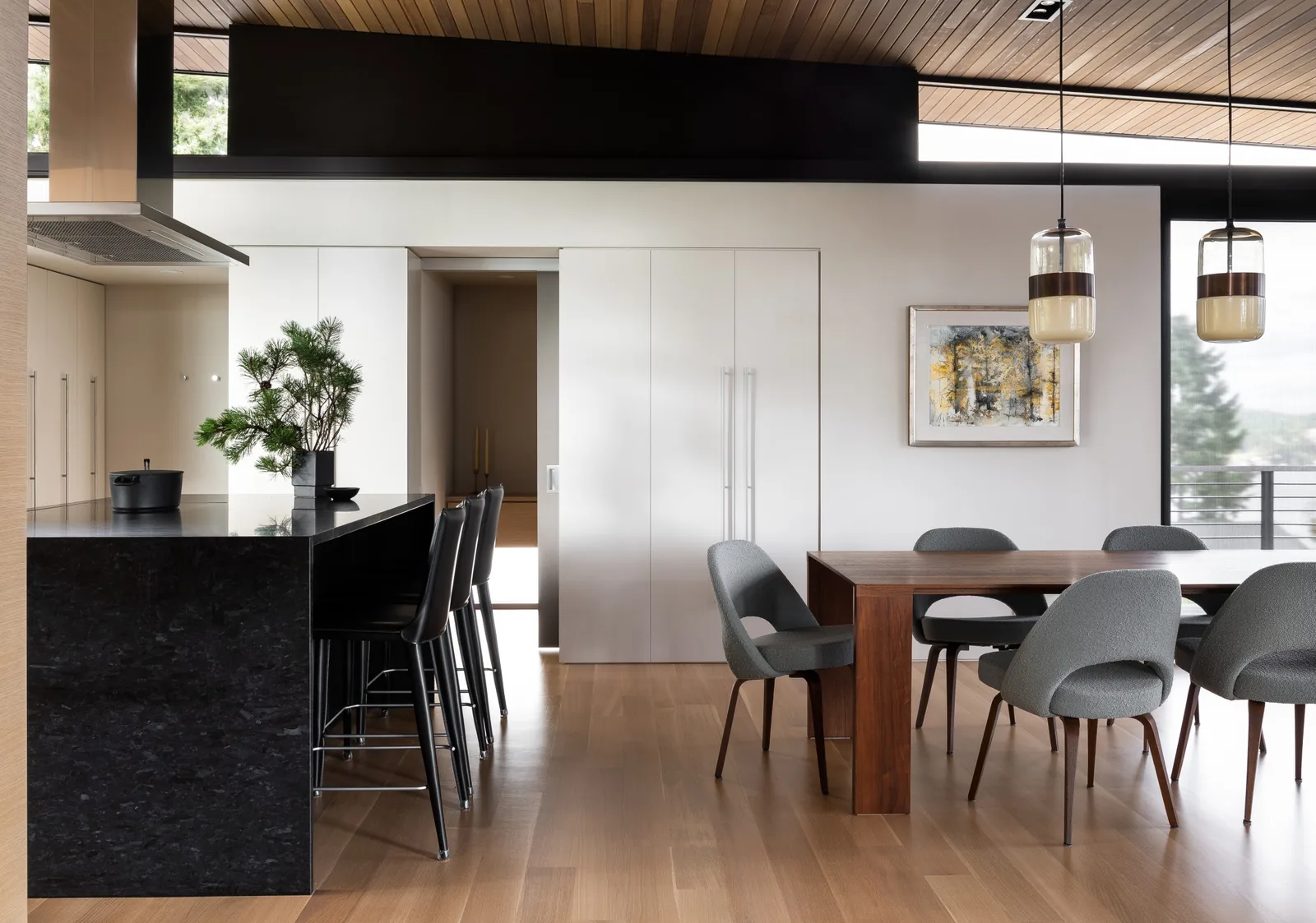 Interior view showing kitchen island with bar stools and adjacent dining table with chairs under two pendant lights.