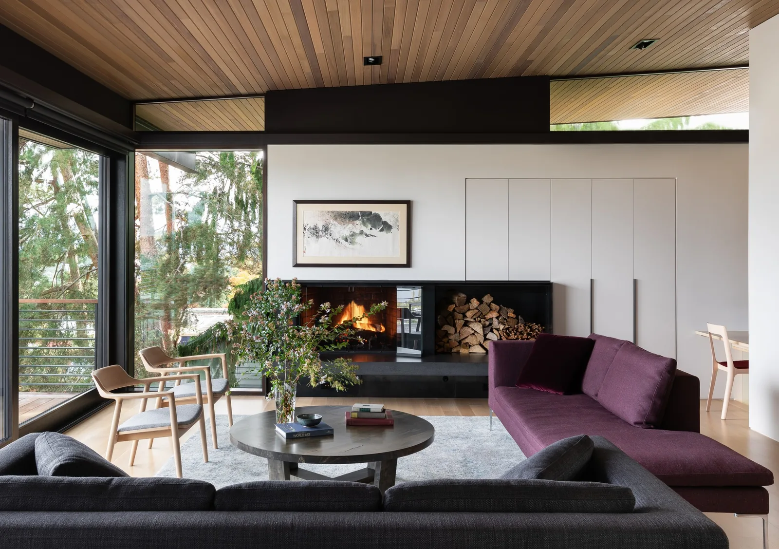 View of a living room featuring a fireplace with adjacent firewood storage and large windows.