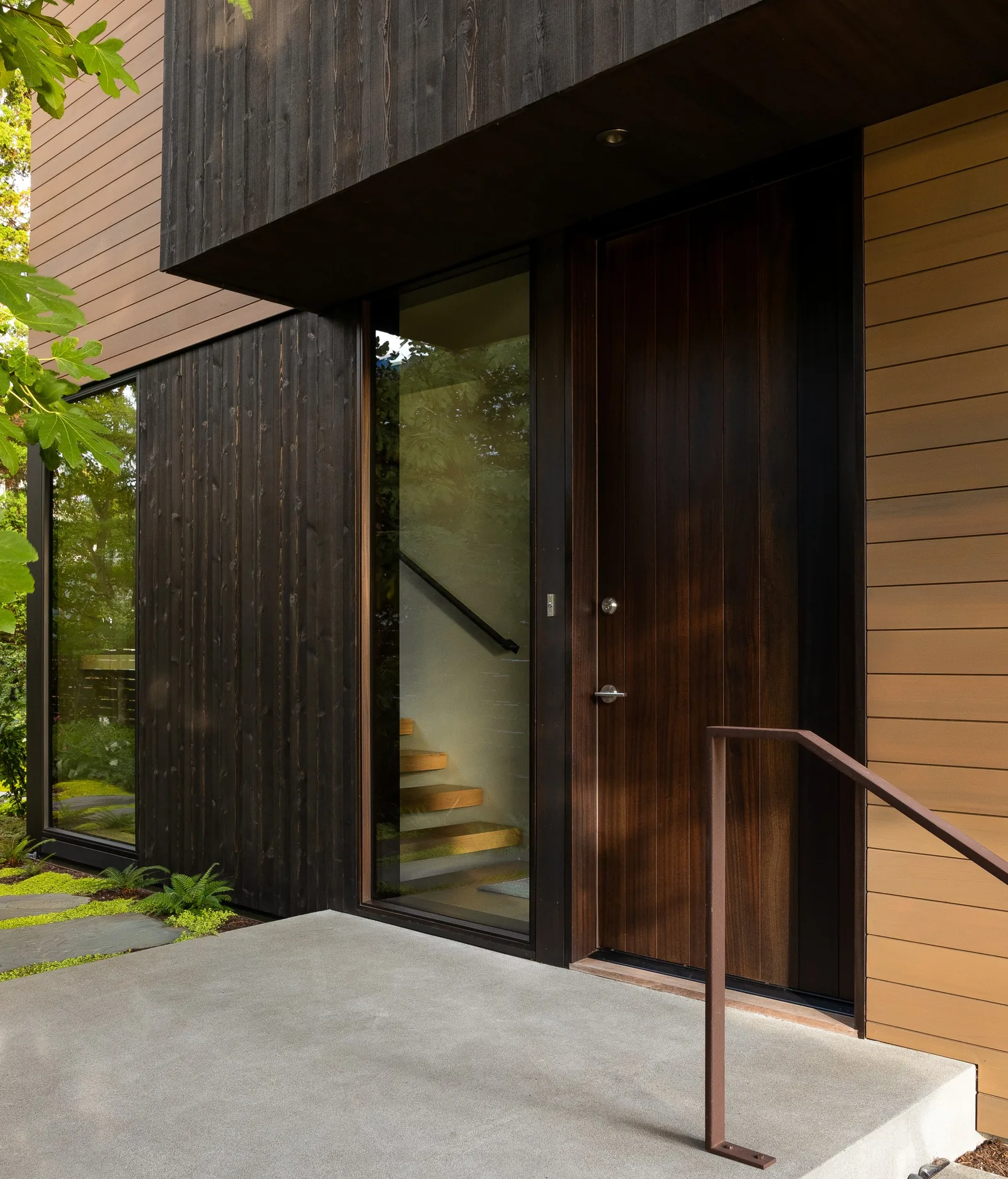 Entry view showing a dark wood panel door and adjacent large glass window with interior staircase visible.