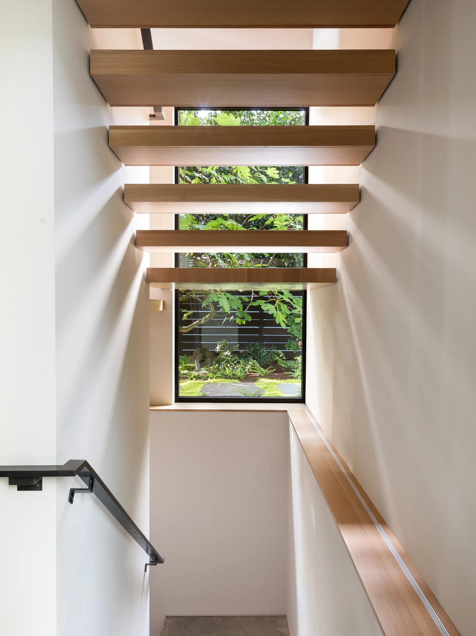 View of a stairwell with horizontal wooden ceiling beams and a framed window looking out to a garden.