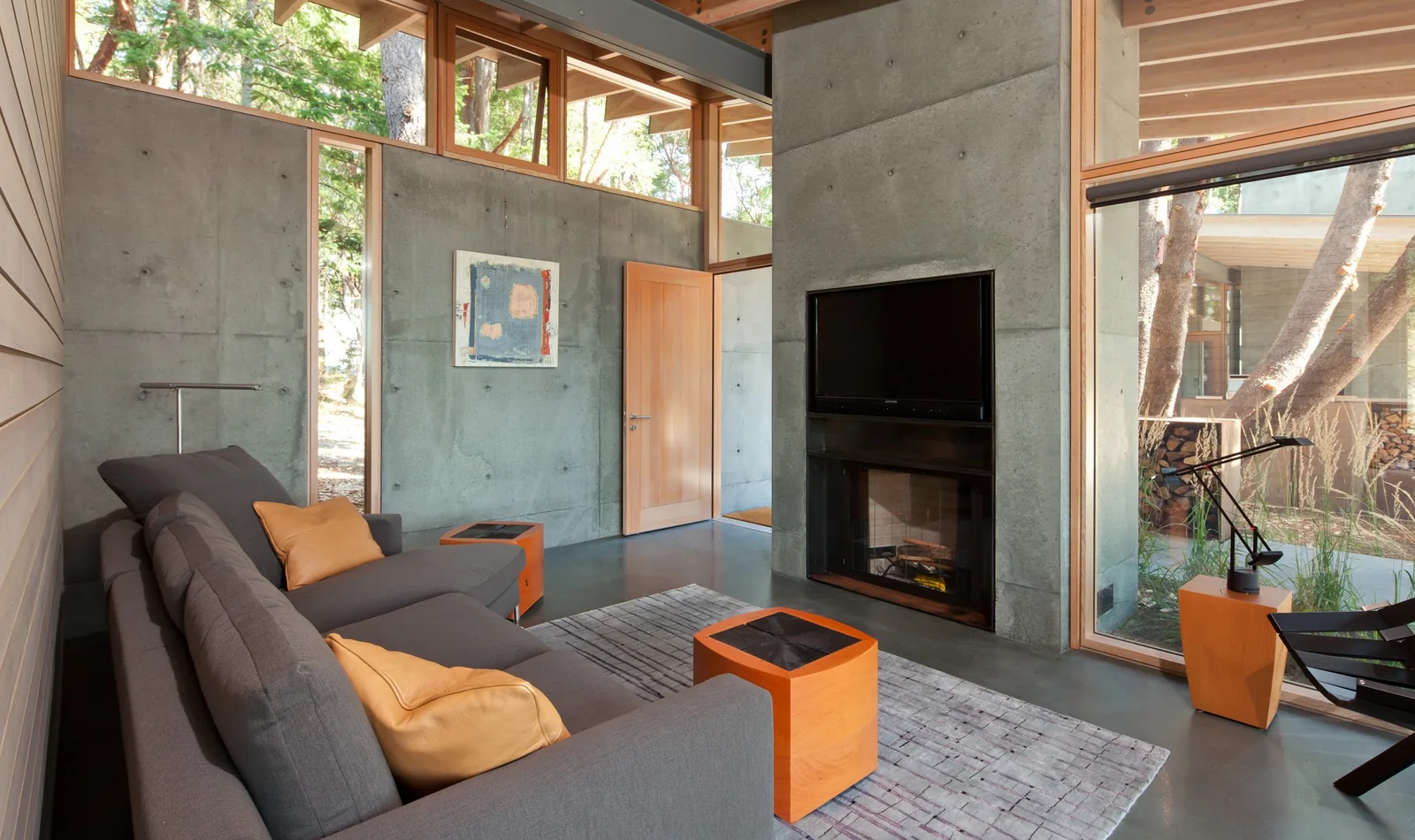 Living room featuring concrete construction with wood trim, a sectional sofa, fireplace, and large windows.