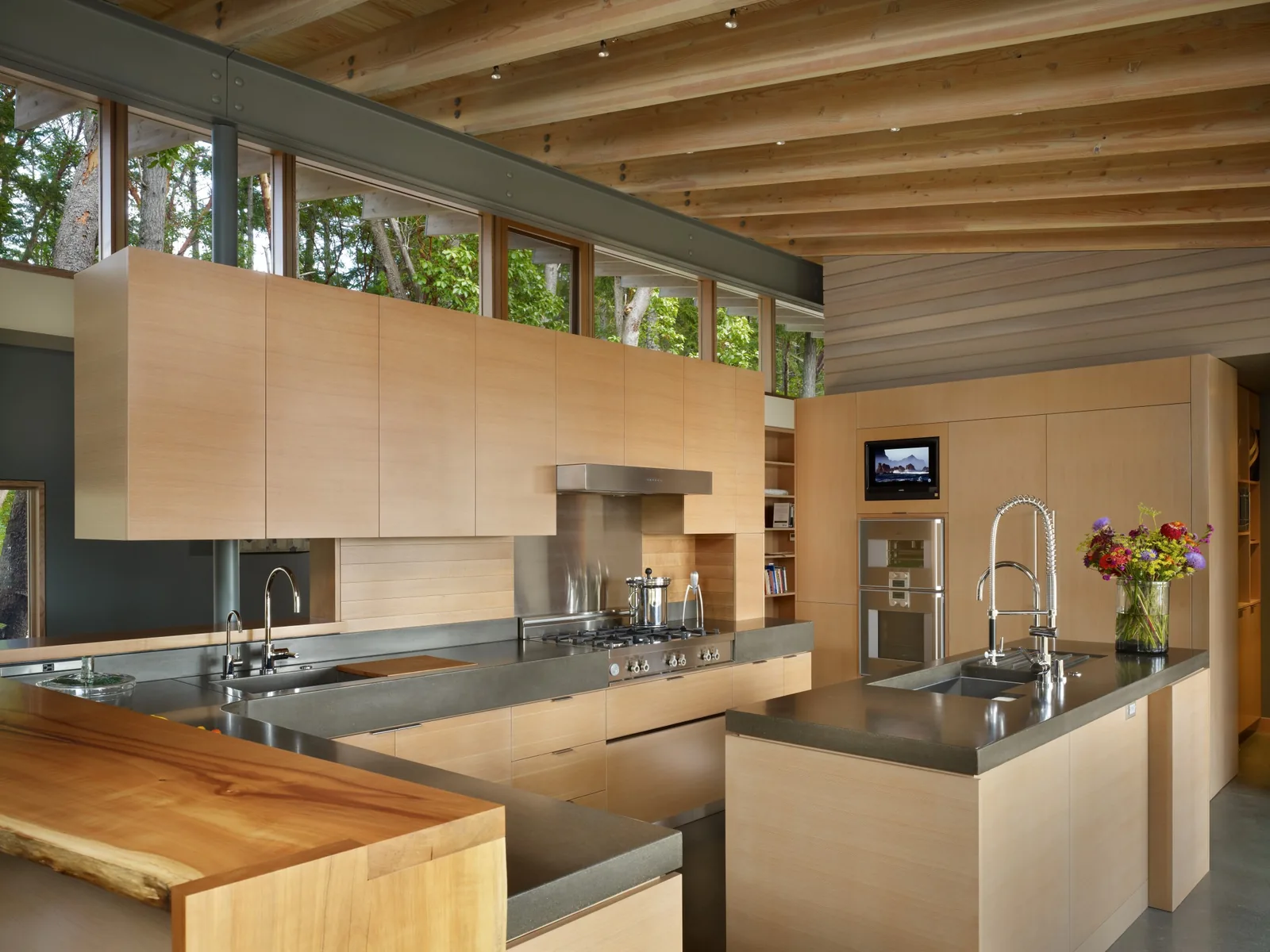 Kitchen featuring light wood cabinets, concrete countertops, and exposed wooden ceiling beams with upper windows providing natural light.
