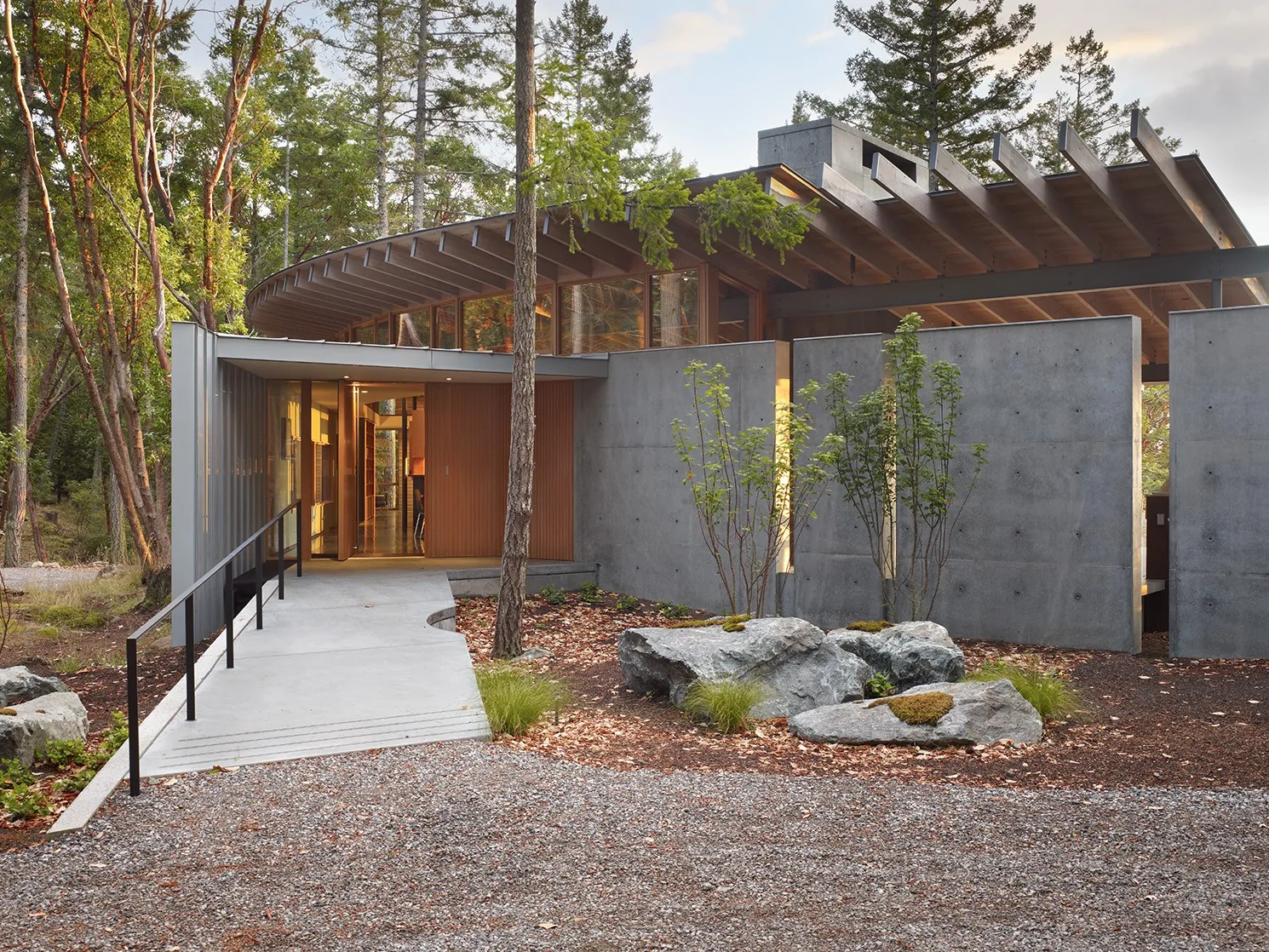 Exterior front view of a modern house featuring a curved wood pergola roof and concrete walls.
