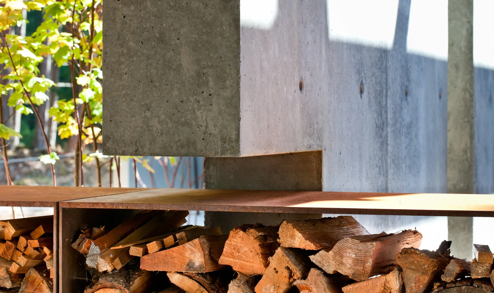 Firewood neatly stacked beneath a minimalist concrete and rusted metal architectural element.