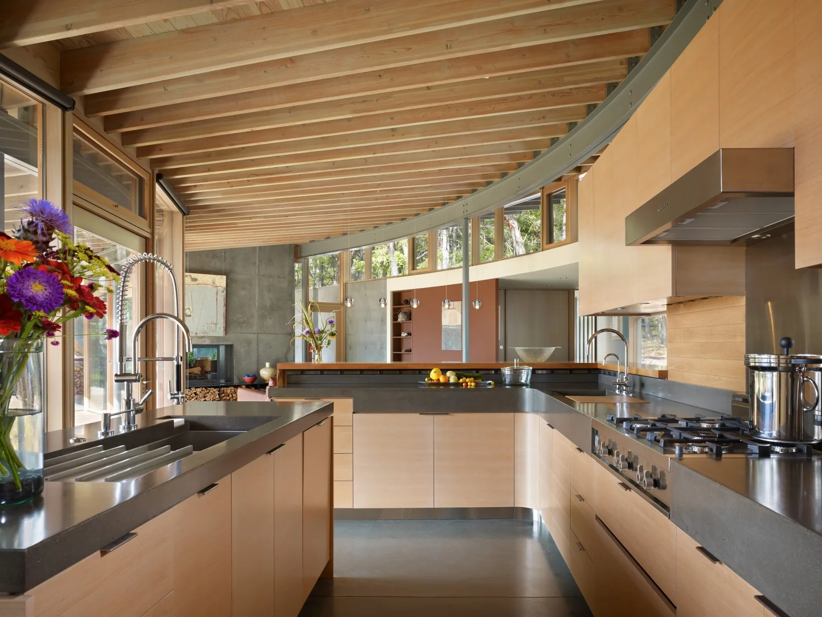 Interior view of a contemporary kitchen with curved wooden ceiling beams and floor-to-ceiling glazing.