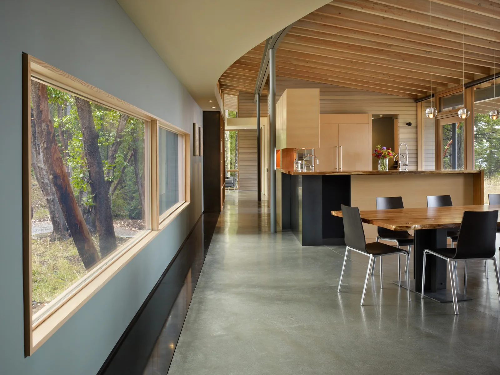 Modern kitchen and dining area with polished concrete floor and large horizontal windows.