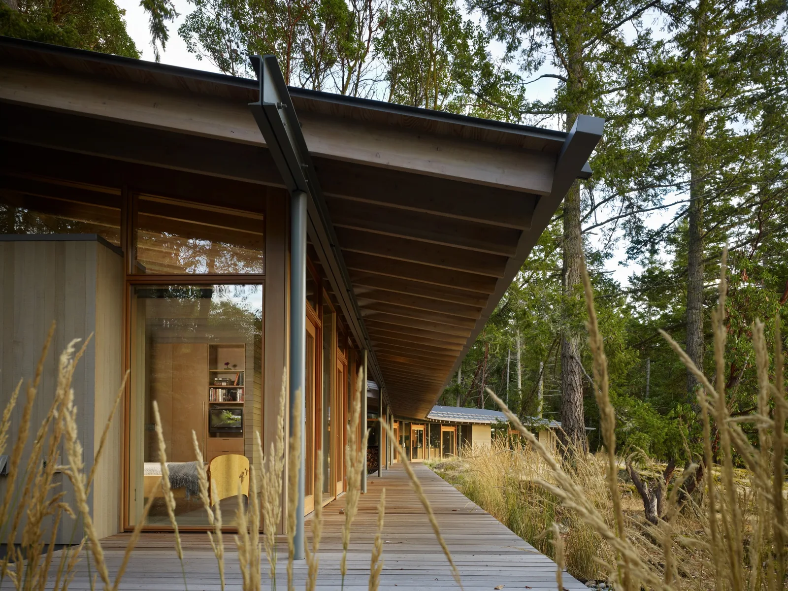 Side exterior view of a wooden house with floor-to-ceiling glazing and an extended eave roof.