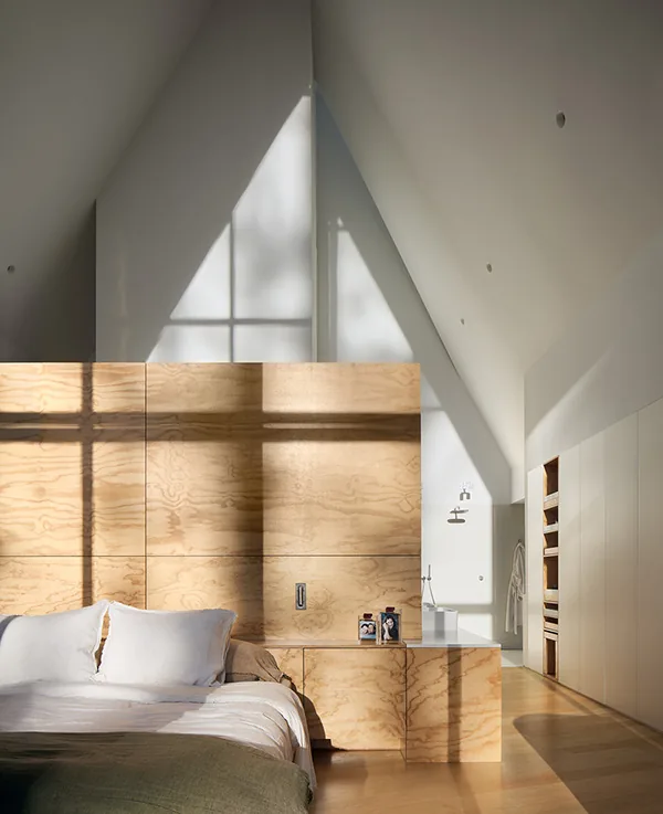 Bedroom with natural wood partition under steeply angled ceiling illuminated by window shadows.