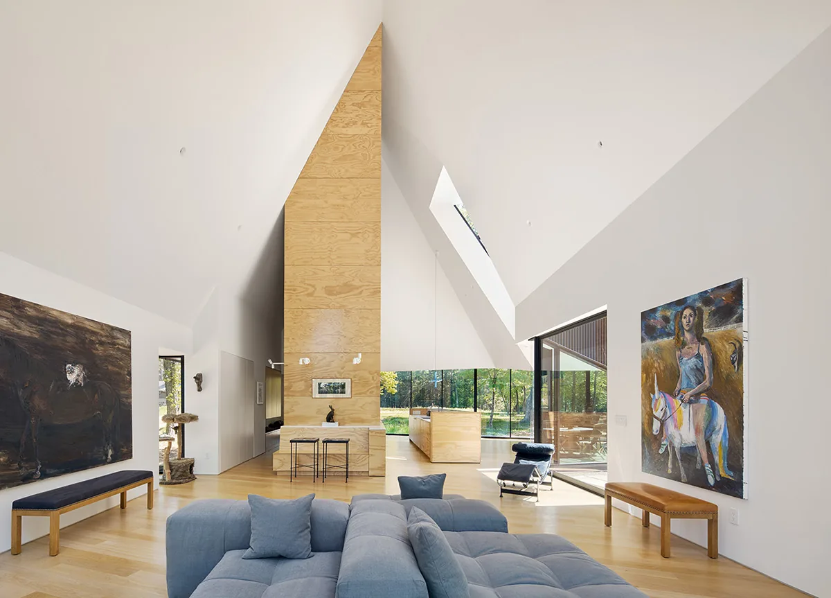 Living room with vaulted ceiling, floor-to-ceiling glass doors, and plywood central chimney enclosure.