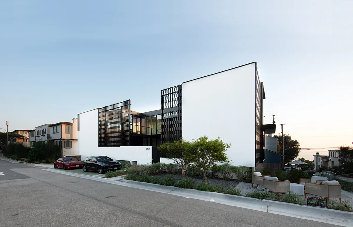 Exterior front and side view of the Alma Switch House showing white stucco walls, black metal screen panels, and landscaping with seating area.