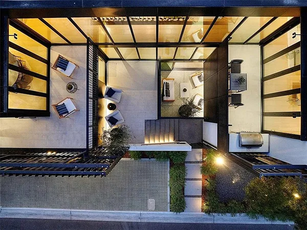 Aerial photo showing a courtyard with seating areas, stairs, and glass-enclosed adjacent rooms at dusk.