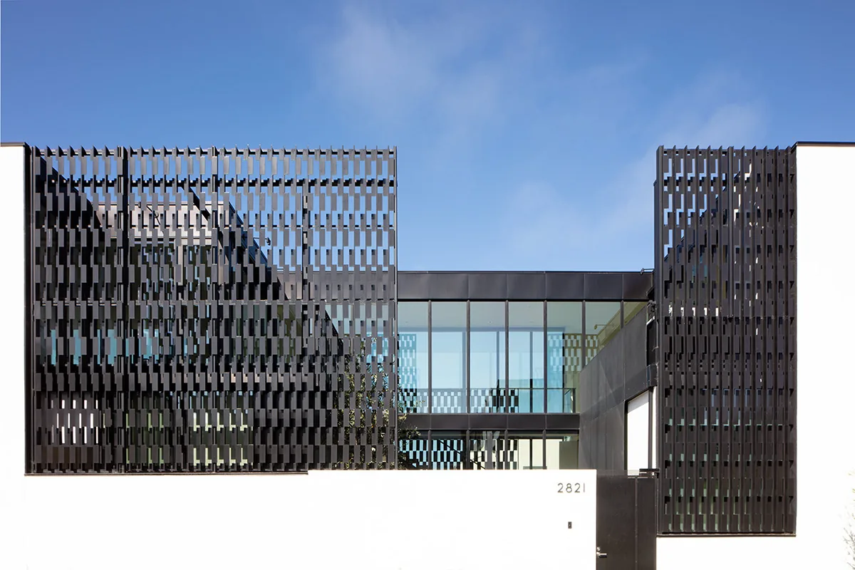 Modern house exterior with black metal perforated screens and large glass windows over a white base wall.