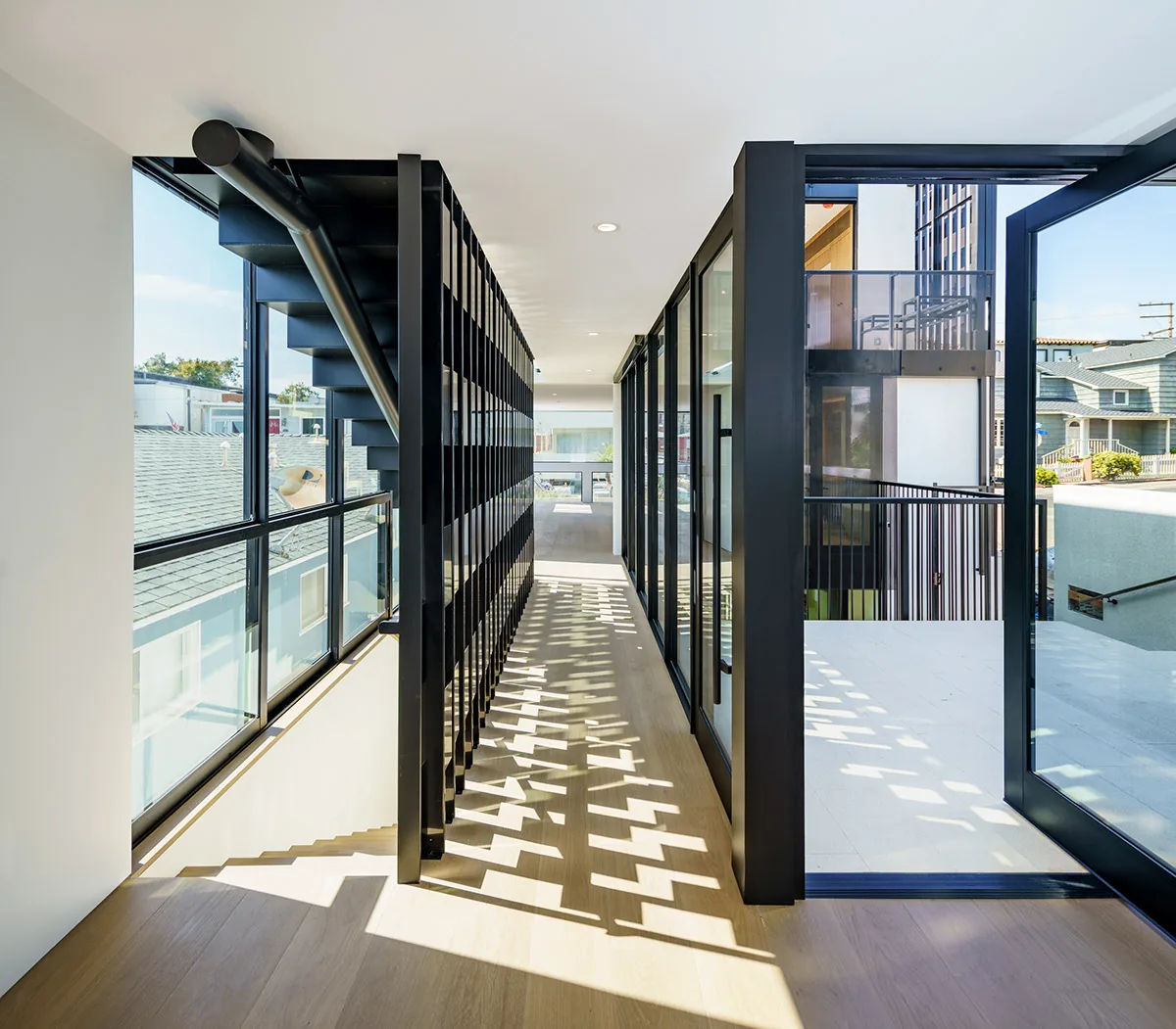 Second-floor corridor with black steel staircase and glass walls allowing natural light to create patterned shadows on the floor.