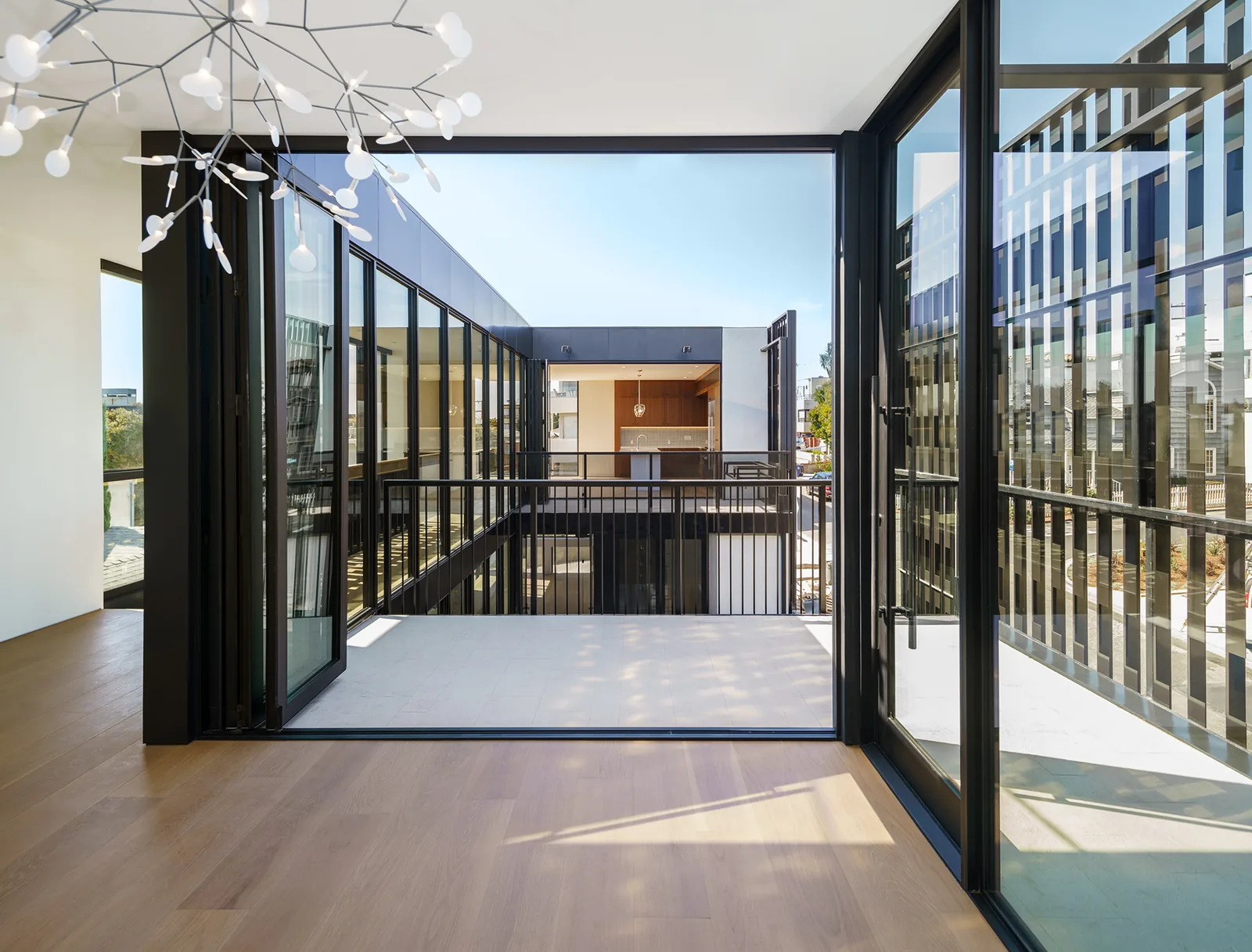 Interior space with hardwood flooring opens through folding glass doors to a balcony overlooking a courtyard with adjacent building across.