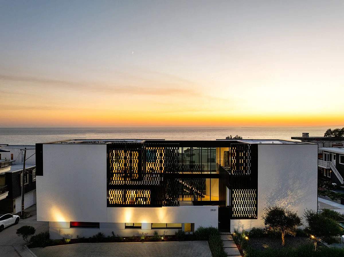 Alma Switch House with illuminated perforated screens and ocean backdrop at sunset.