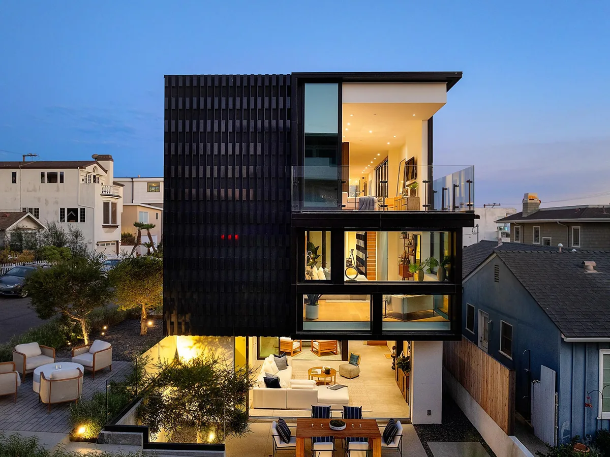 Three-story modern house featuring large glazing and a nighttime view of the illuminated interior and outdoor spaces.