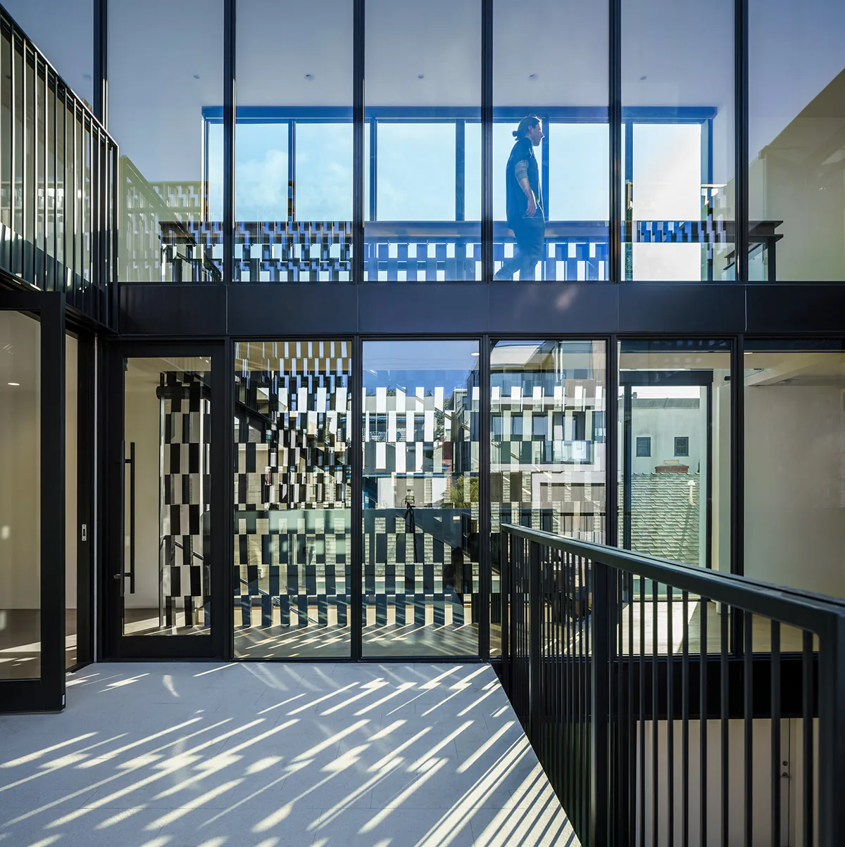Interior courtyard area with floor-to-ceiling glazing and metal railings, featuring patterned shadows from the screen elements.