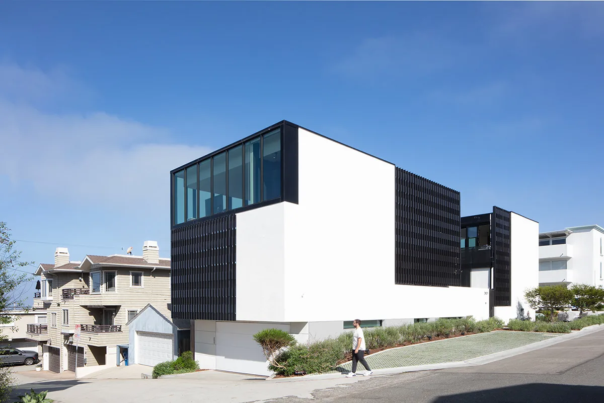 Exterior front view of the Alma Switch House showing its white stucco walls and black metal screening on a sloping street.