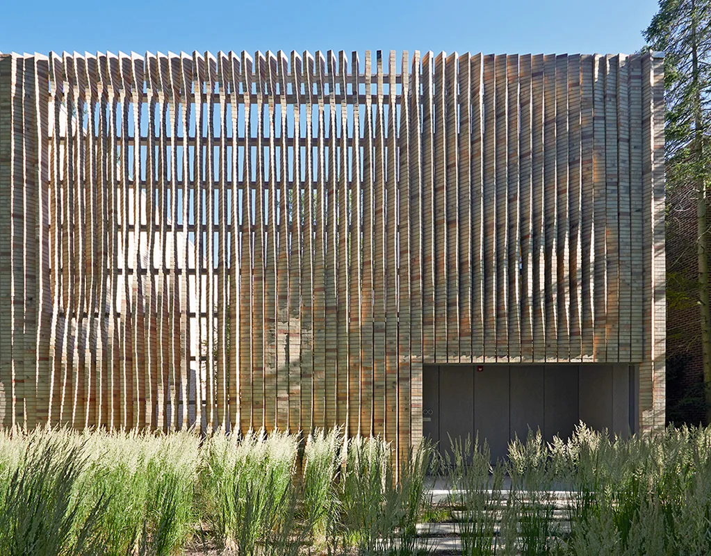 Cube-shaped house with vertical wood slat facade and a flat roof, surrounded by landscaping.
