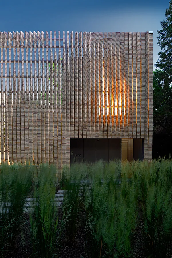 Exterior of the Lipton Thayer House featuring a vertical wood slat facade and floor-to-ceiling glazing behind it, with dense green grasses in the foreground.