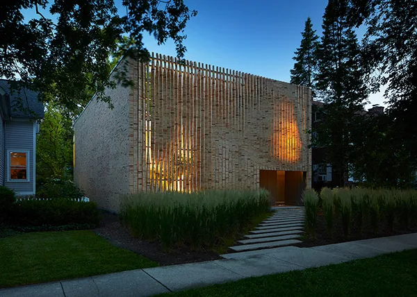 The Lipton Thayer House features a textured brick facade with vertical wood slats and a flat roof, set among green grasses.