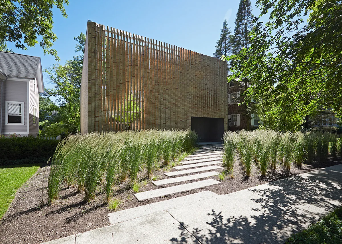 The Lipton Thayer House features a cubic shape with a textured vertical brick slat facade and a flat roof, set among dense green grasses.