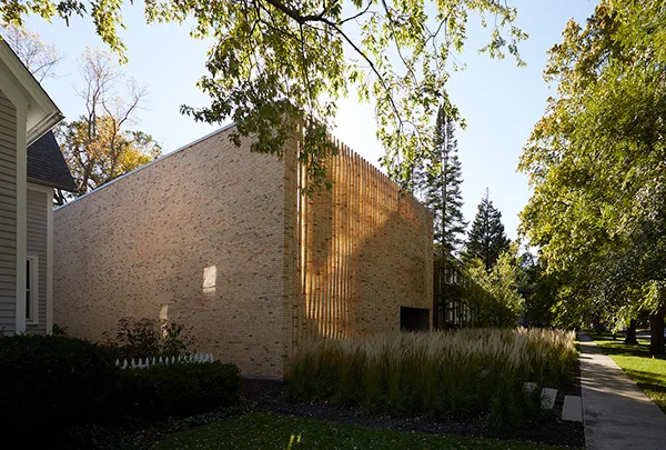 Lipton Thayer House features a cube-shaped brick exterior with vertical wood slats, set in a landscaped yard with mature trees.