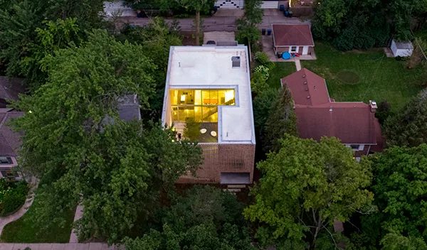 Aerial view of the Lipton Thayer House showing its modern cube form with illuminated interior and surrounding green lawn and trees.