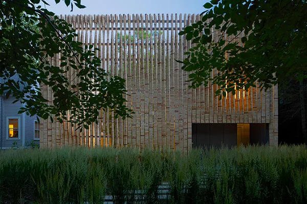 The cube-shaped Lipton Thayer House features a textured facade of vertical wood slats and a flat roof as seen at dusk.