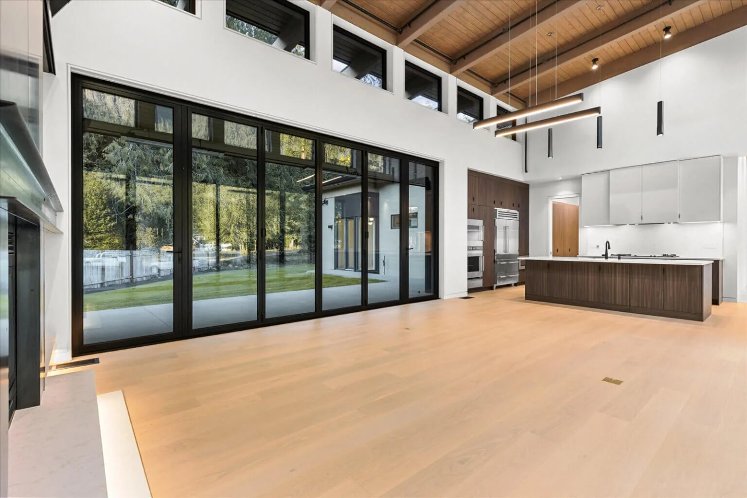 Open kitchen and living space features floor-to-ceiling glass sliding doors and clerestory windows beneath a vaulted wood ceiling.