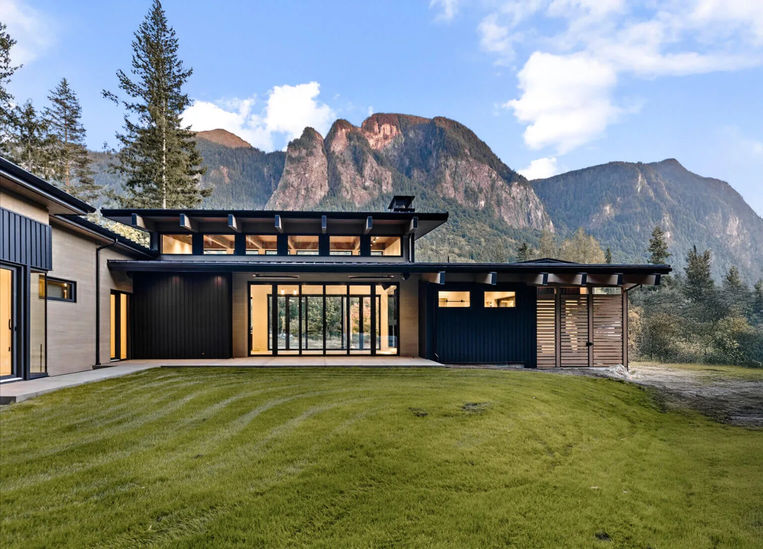 Rear exterior of Echo Ridge House featuring extensive glazing, wood and black cladding, and a mountain backdrop.