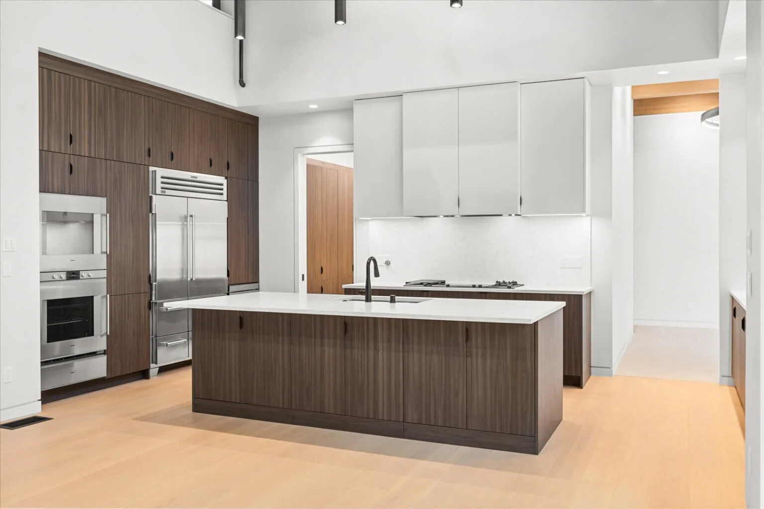 Kitchen with dark wood lower cabinets, white upper cabinets, a large island with sink, and stainless steel appliances.
