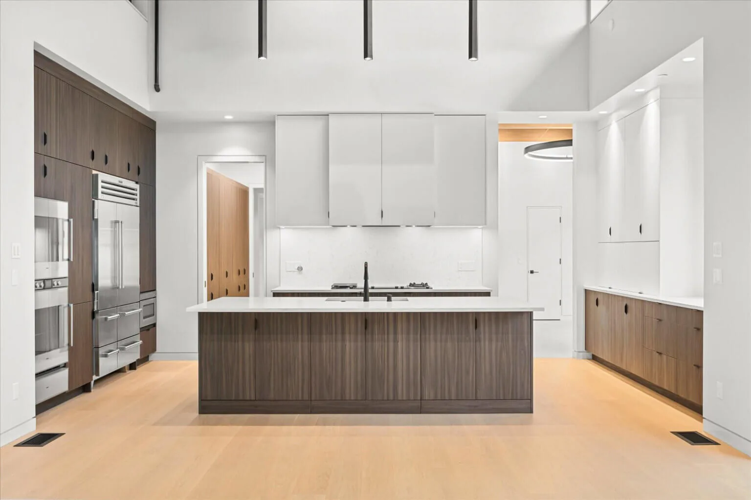Kitchen featuring a large central island with dark wood cabinetry, built-in stainless steel appliances, and white upper cabinets.